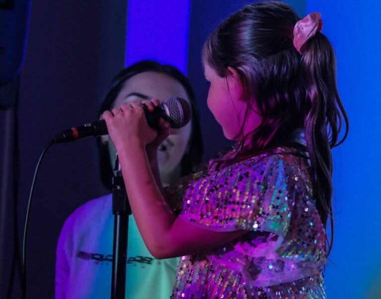 Young singing student on stage with supportive singing coach under gorgeous purple and blue lights